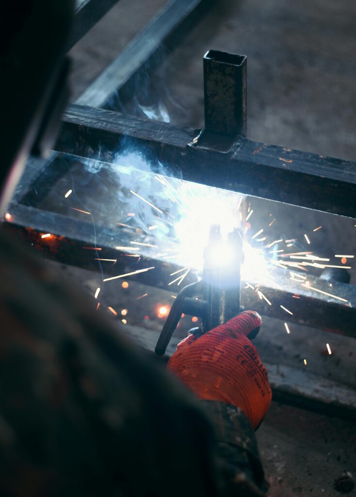 Welding sparks fly as industrial worker welds metal in a factory.