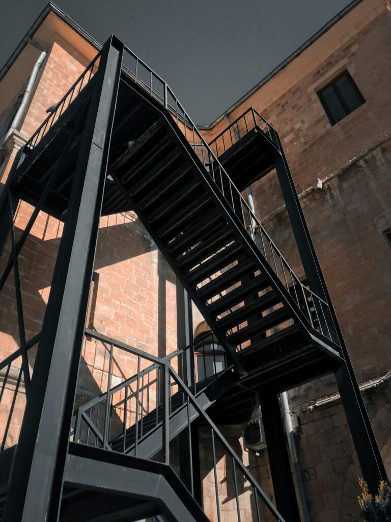 Low-angle shot of a black metal staircase attached to a brick building, showcasing industrial architecture.